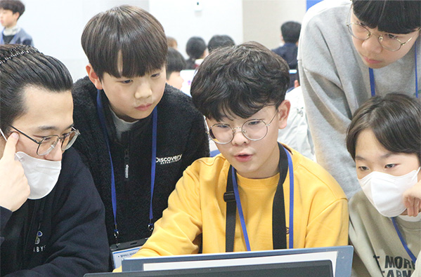 An adult and several children learning together while looking at a computer monitor